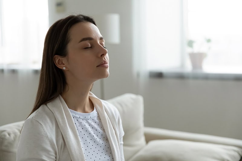 woman taking a deep breath in her living room.